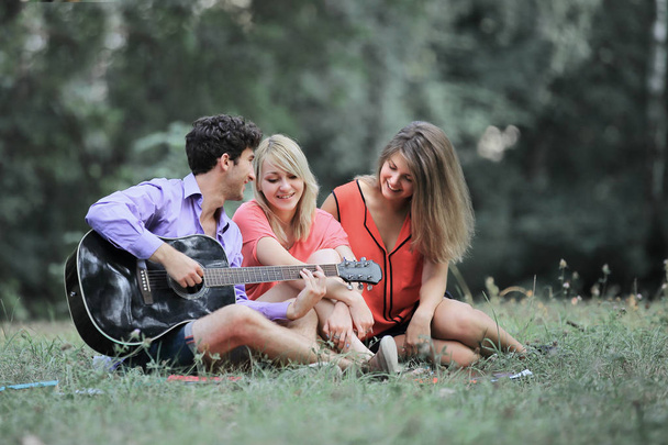 Skupina studentů s kytarou relaxovat, sedět na trávě v city parku - Fotografie, Obrázek