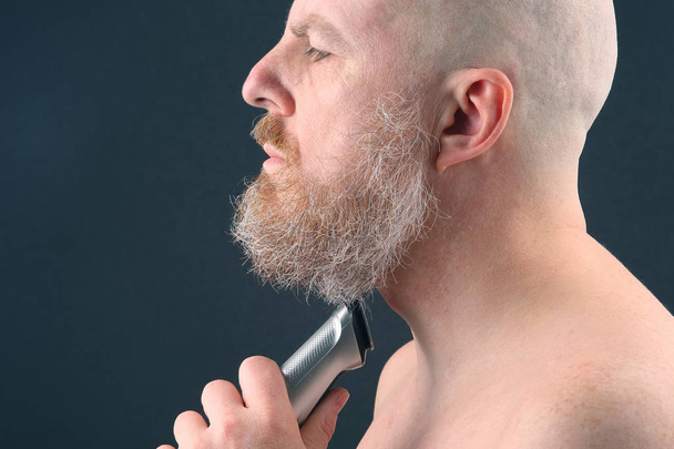 Bearded man with trimmer to adjust beard in hand - Foto, Bild