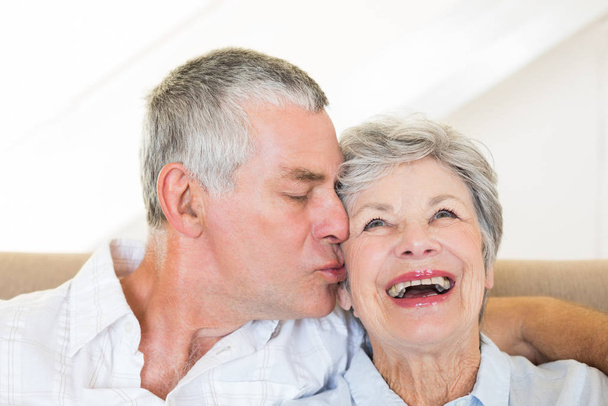 Senior man kissing happy wife sitting on sofa at home - Φωτογραφία, εικόνα