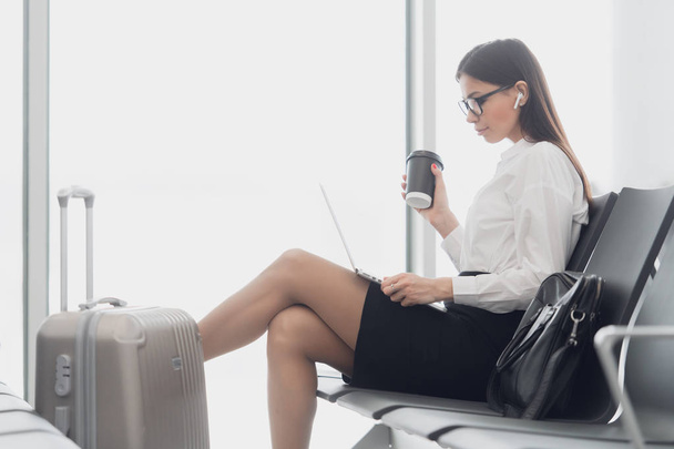 Mujer disfruta del ordenador portátil y bebe café en la terminal del aeropuerto
 - Foto, imagen