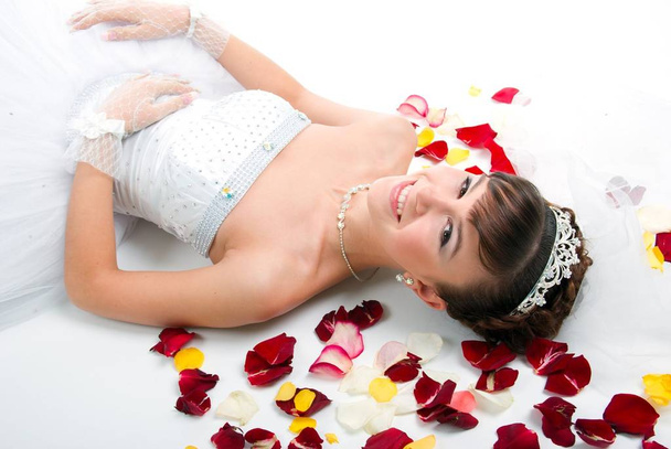 Beautiful sexy bride on  floor among red rose petals on white background - Fotó, kép