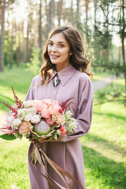 Beautiful model girl with brown hair in stylish pink dress holding bouquet of flowers at a wedding ceremony - Foto, Bild