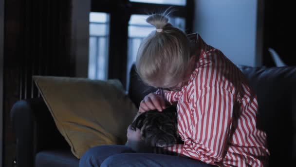Młoda piękna kobieta wieje pocałunek do swojego psa mopsa na kanapie, Cute Mops całuje dziewczynę, pies i właściciel siedzi na czarnej kanapie - Materiał filmowy, wideo