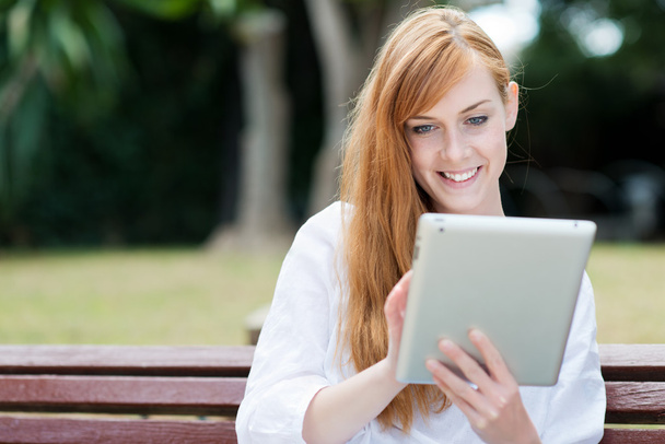 jonge vrouw zitten in een park met haar tablet-pc - Foto, afbeelding