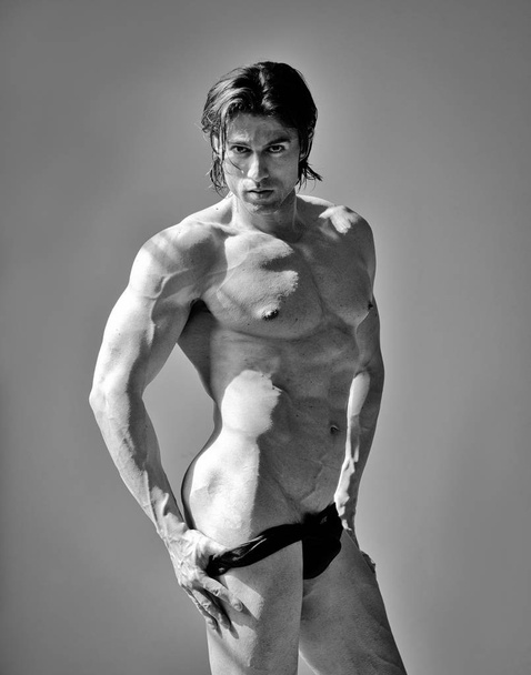Handsome muscular man shirtless pulling down underwear, on grey background - Fotografie, Obrázek