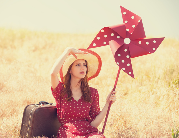 Redhead girl with suitcase and wind turbine sitting at grass - Photo, Image