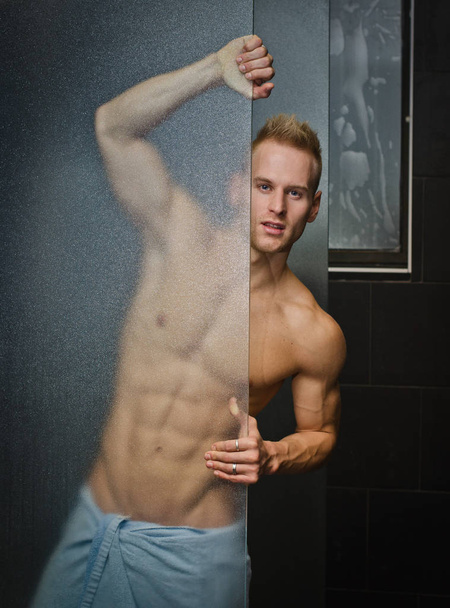 Handsome young man shirtless behind shower glass, with towel around waist - Foto, Bild
