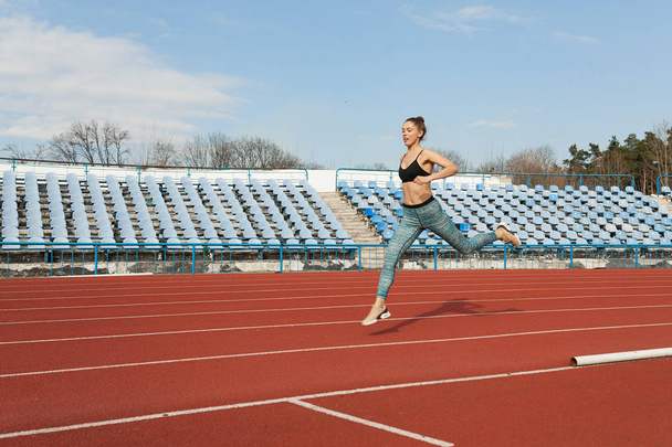 Young woman running during sunny morning on stadium track - Zdjęcie, obraz