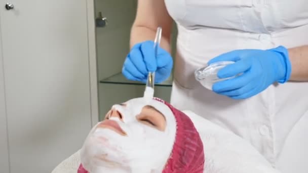 Yüze beyaz anti-aging maskesi uygulayan güzellik uzmanı. Güzellik konsepti. Spa merkezinde 30'lu yaşlarda genç bir kadın yüz germe işlemi yaptırıyor. Yakından kapatın. Hd - Video, Çekim
