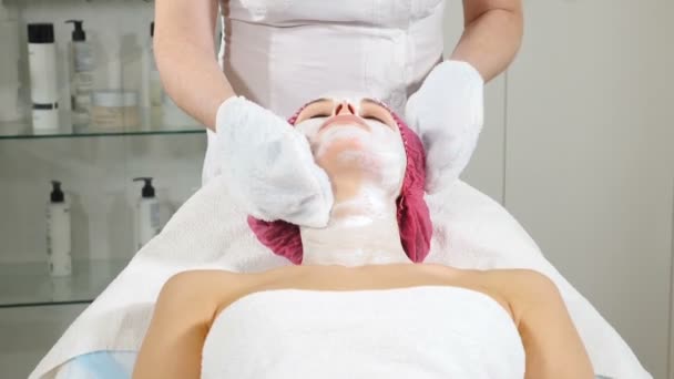 Vrouwelijke cosmetoloog veegt gezicht na een Beauty masker uit vrouwelijke cliënt. Close-up. Vrouw krijgt huidbehandeling in moderne salon. Hd - Video