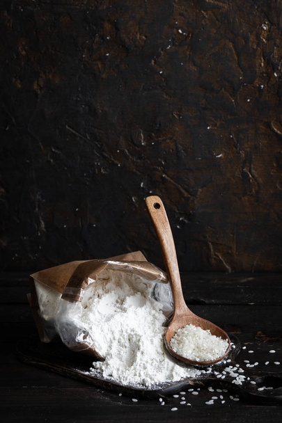Harina de arroz blanco en una bolsa de elaboración sobre un fondo de madera oscura
 - Foto, imagen