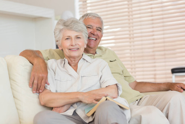 Cheerful senior couple relaxing on the couch together at home in the living room - 写真・画像