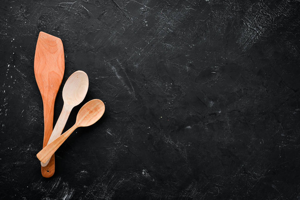 Wooden kitchen utensils. On a black stone background. Top view. Free copy space. - Foto, imagen