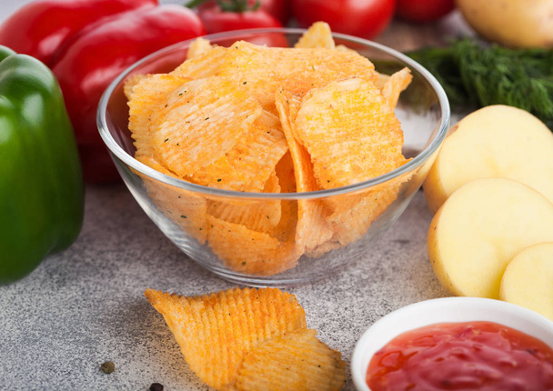 Glass bowl plate with potato crisps chips with paprika on light table background. Red and green paprika pepper with potatoes and sweet chilli sauce. - Фото, изображение