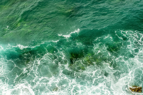 Meereswellen brechen an den Steinen der Küste auf. das wütende Meer und der Schaum. Blick von oben. grüner Hintergrund. - Foto, Bild