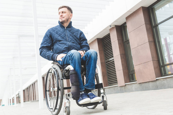 Young man in a wheelchair against the backdrop of a modern high-rise building. - Фото, изображение