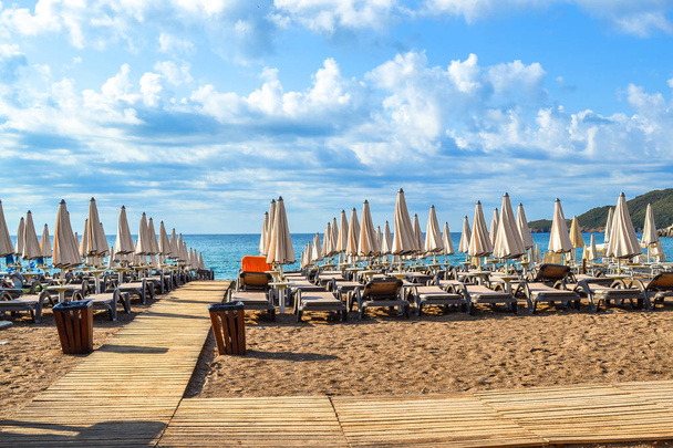 Plaża Czarnogóry. Leżaki i parasole w stanie zmontowanym na plaży. Chmury nad morzem. Riviera Budva. W mieście vecici - Zdjęcie, obraz