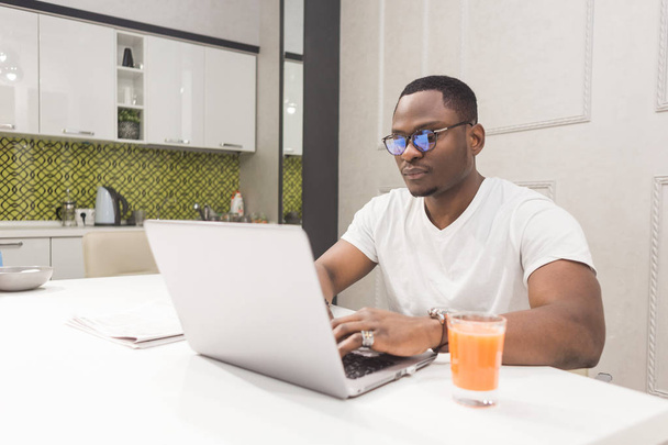 Young African American businessman working on a laptop in the kitchen in a modern interior. - Foto, Imagem