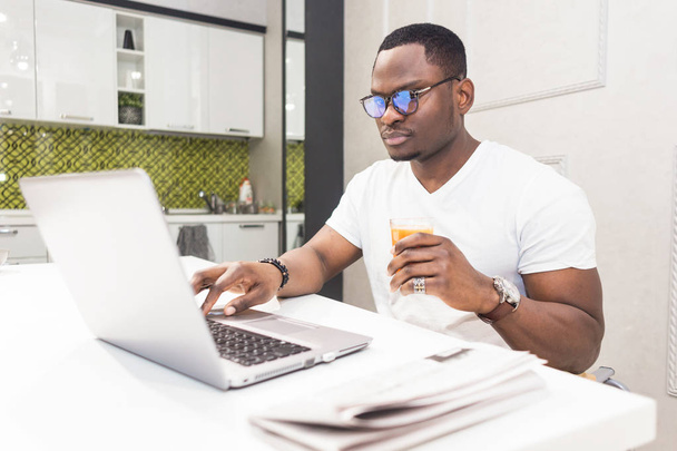 Young African American businessman working on a laptop in the kitchen in a modern interior. - Foto, immagini