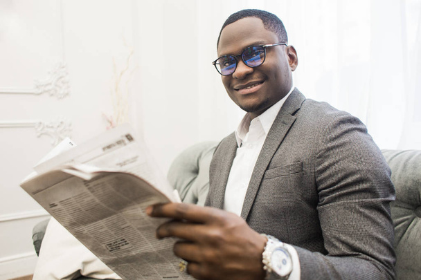 Молодих афро-американських бізнесменом у сірому костюмі, читаючи газету, сидячи на дивані. - Фото, зображення