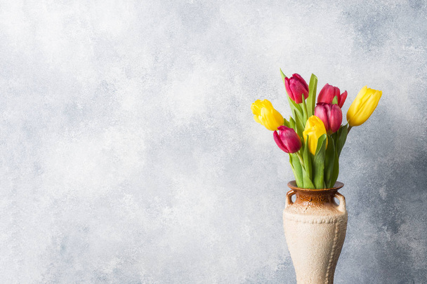 Bouquet of yellow and pink tulips in vase on a gray background. Copy space for product and text. - Фото, зображення
