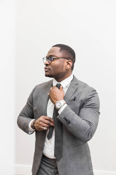 Young African American businessman in a gray suit tying a tie on a white background. - Foto, immagini