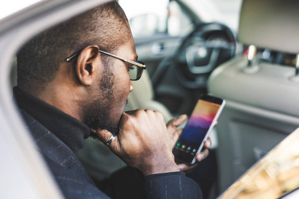 Young successful businessman talking on the phone sitting in the backseat of a expensive car. Negotiations and business meetings. - Foto, imagen