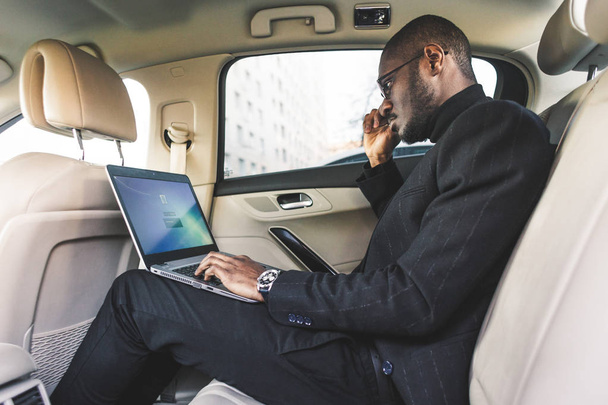 Man in a business suit write on laptop in the salon of an expensive car with leather interior. - Foto, Bild