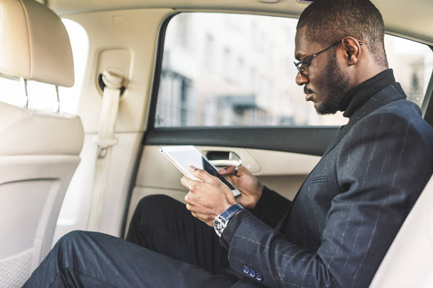 Young businessman using tablet while sitting in the backseat of a car. - 写真・画像