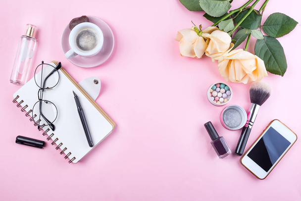 Workplace mockup with notebook, glasses, roses, phone and accessories on pink background top view. Flat lay with coffee copy space. Feminine working style concept. - Photo, Image