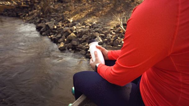 Кавказка в ярком шлеме спортивной обуви лежит на мосту через реку. Велосипедист в яркой спортивной одежде с фляжкой и пластиковой бутылкой в руке. Отдых перерыв пить воду жажду
 - Фото, изображение