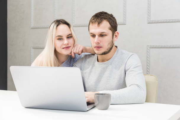 Young couple sitting at the morning in they kitchen and using laptop. Online shopping concept. Modern kitchen in background. - Foto, afbeelding