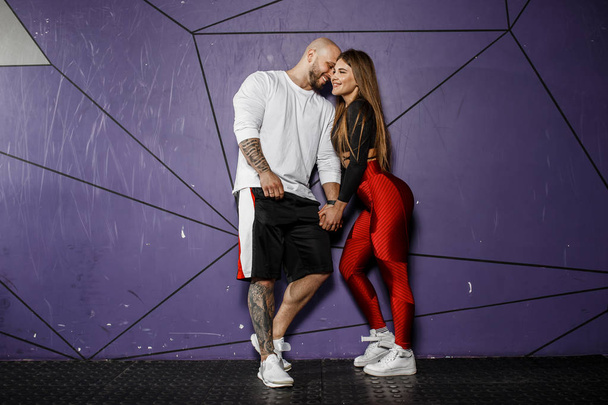 Cute athletic couple. Slender beautiful girl and strong athletic man in sports clothes are hugging on the background of stylish violet wall - Foto, Imagem