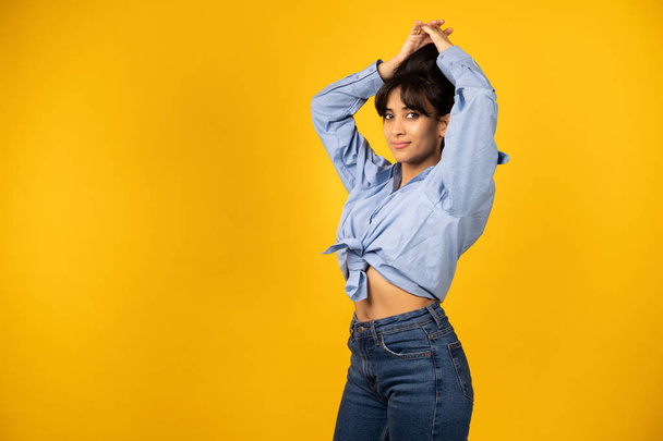Young beautiful girl in a blue shirt posing for a photo on a yellow background. - Photo, Image