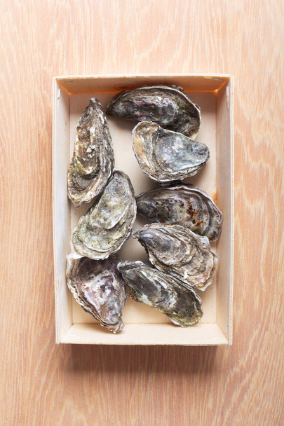 Closed oysters in a box on wooden background. Healthy sea food - Photo, image