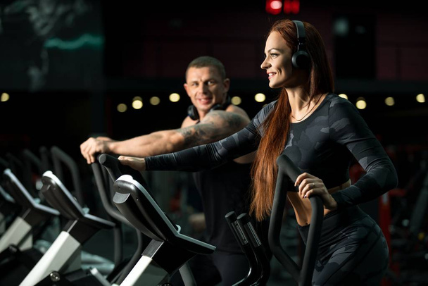 Homem e mulher se exercitando em simuladores em um ginásio
 - Foto, Imagem