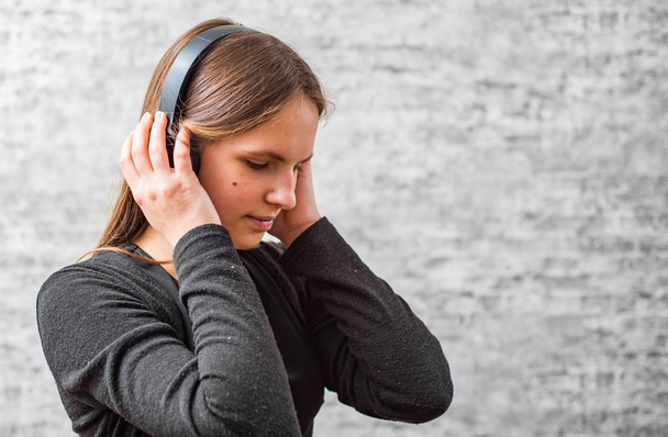 ritratto di giovane adolescente ragazza bruna con i capelli lunghi ascoltare musica su cuffie wireless su sfondo grigio parete
 - Foto, immagini