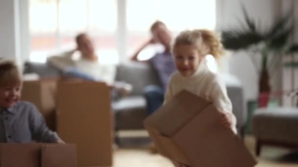 Playful happy kids playing game holding boxes on moving day - Footage, Video