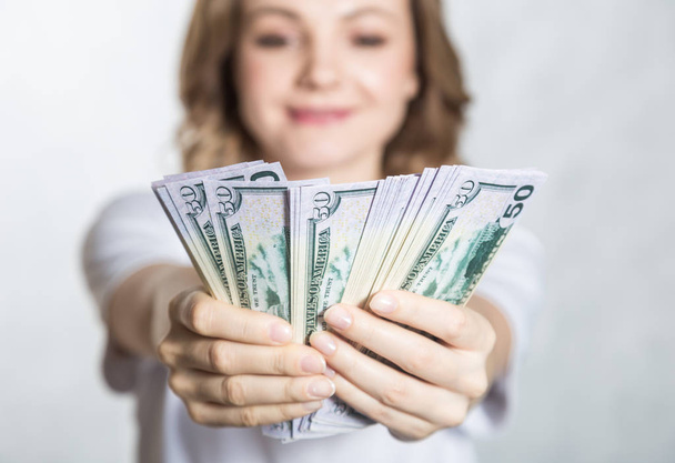 Szczęśliwy młody uśmiechnięta kobieta trzymać nam pieniądze dolara w ręku na białym tle. - Zdjęcie, obraz