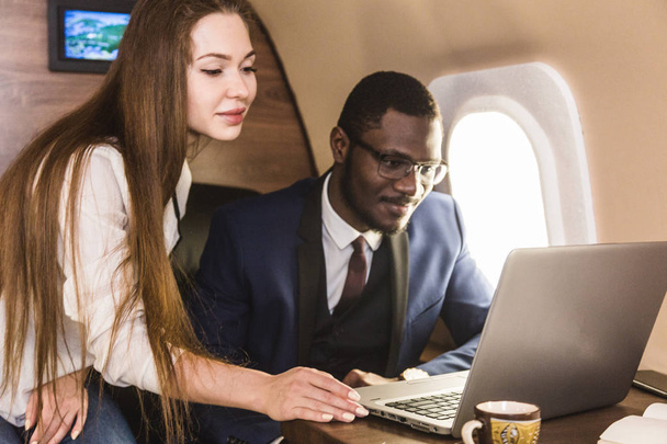 Young successful African-American businessman with glasses and an attractive female workmate blonde in a private jet. Service and flight first class - Photo, Image