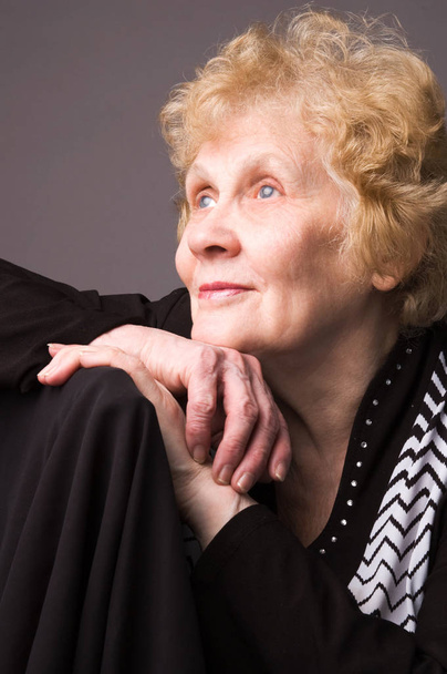The elderly woman in a black dress on a grey background. - Valokuva, kuva