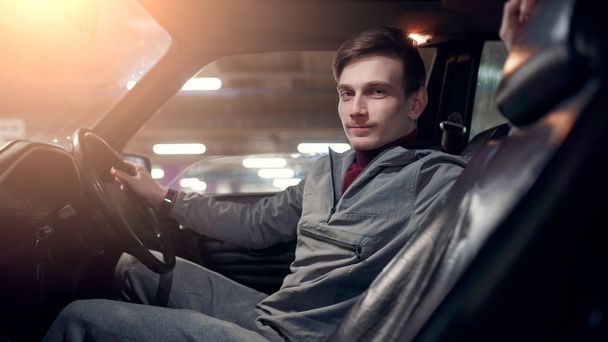 Photo from side of man looking at camera sitting in car on underground insurance - Фото, зображення