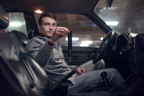 Photo of side of man driver holding keys sitting in black car . - Fotoğraf, Görsel