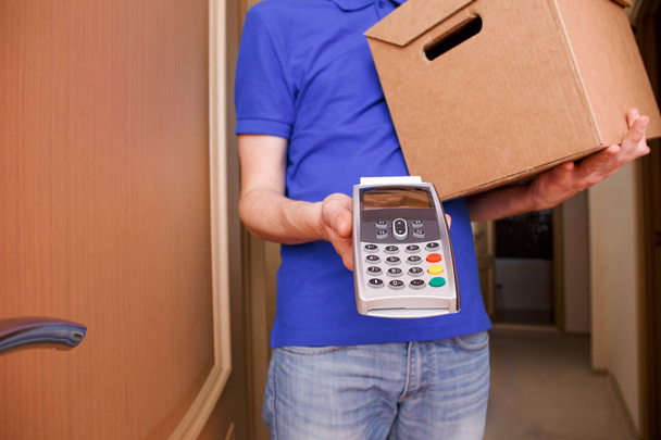 Courier man in blue t-shirt and baseball cap with pin pad and cardboard boxes in hands. - Foto, Imagem