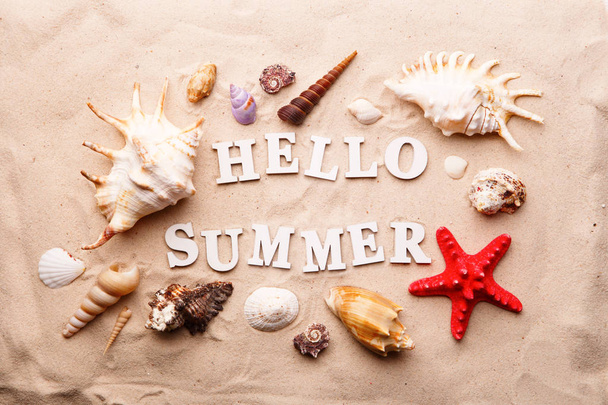 Tekst Hello Summer van witte letters en zeeschelpen en zeesterren op zand - Foto, afbeelding