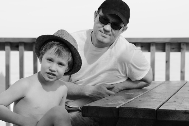 Щасливий батько і його син сидять на літньому кафе на пляжі
 - Фото, зображення
