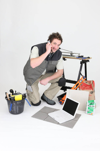 craftsman making a call near laptop and miscellaneous tools - Foto, imagen