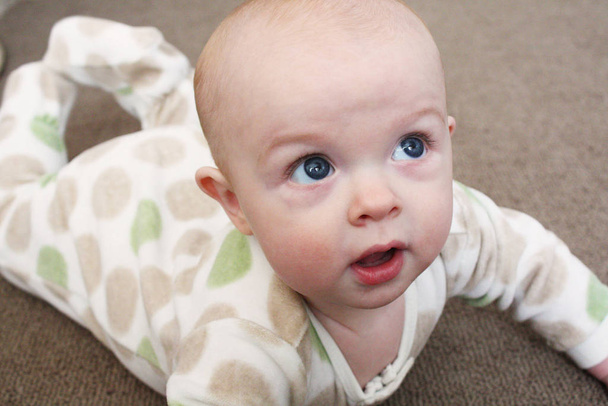 A close-up image of a baby playing on a brown carpet. - Foto, afbeelding