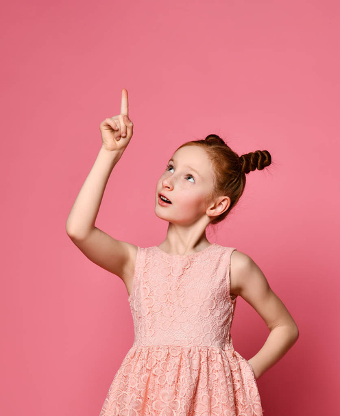 Happy girl redhead in pink dress posing with hand on hip while having an idea and looking at camera - Foto, immagini