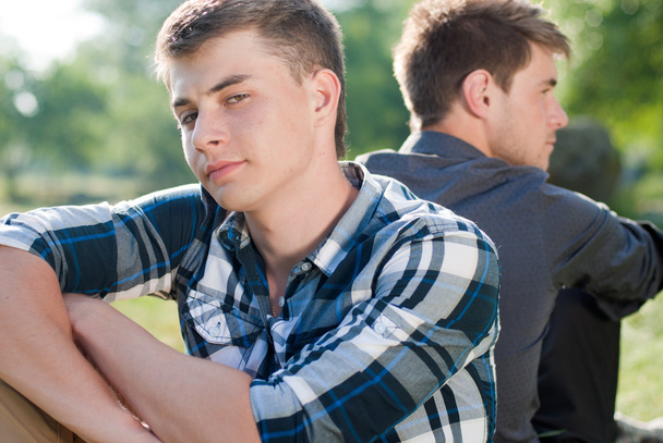 緑の草に一緒に座っている 2 つの若い男性 - 写真・画像